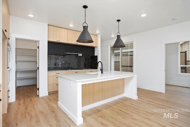 kitchen with gas cooktop, light brown cabinetry, decorative light fixtures, a center island with sink, and light hardwood / wood-style floors