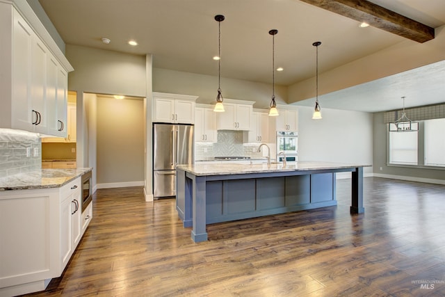 kitchen featuring appliances with stainless steel finishes, beam ceiling, wood-type flooring, a kitchen island with sink, and tasteful backsplash