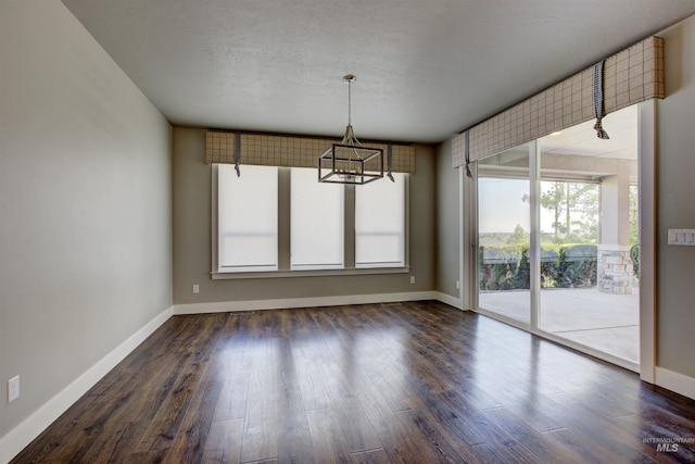 unfurnished dining area featuring a textured ceiling, an inviting chandelier, and dark hardwood / wood-style floors