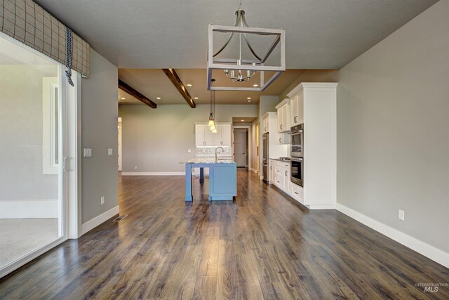 kitchen featuring beam ceiling, a breakfast bar, an island with sink, and hanging light fixtures