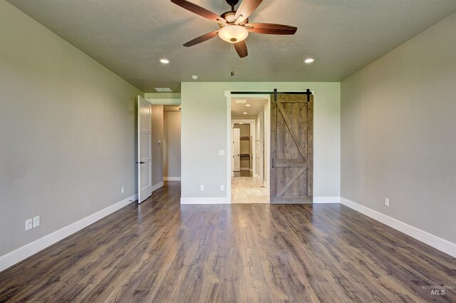 unfurnished bedroom featuring ceiling fan, a barn door, and wood-type flooring