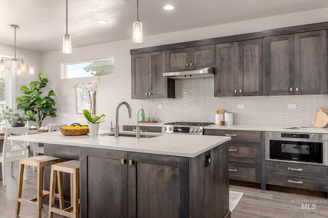 kitchen featuring under cabinet range hood, stainless steel oven, dark brown cabinetry, and a sink