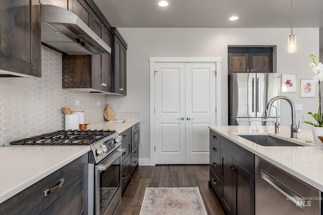 kitchen with light countertops, wall chimney range hood, appliances with stainless steel finishes, and a sink