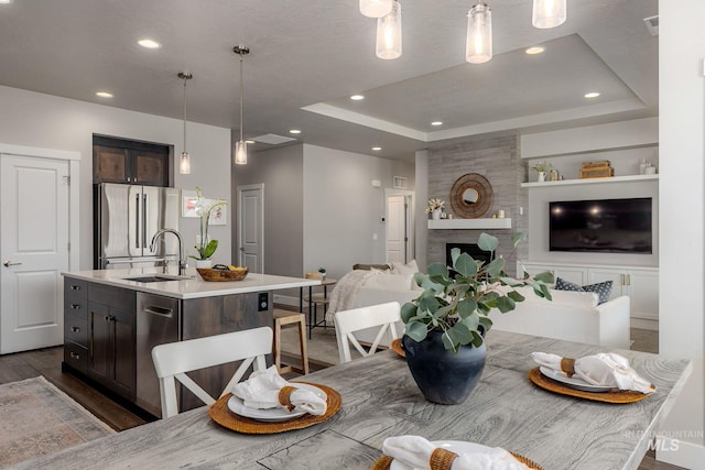 dining area featuring a large fireplace, recessed lighting, a raised ceiling, and dark wood-style flooring