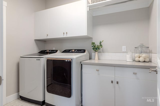 washroom with washing machine and clothes dryer, cabinet space, and baseboards