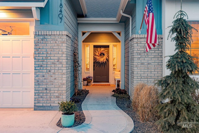 doorway to property featuring an attached garage, brick siding, and roof with shingles