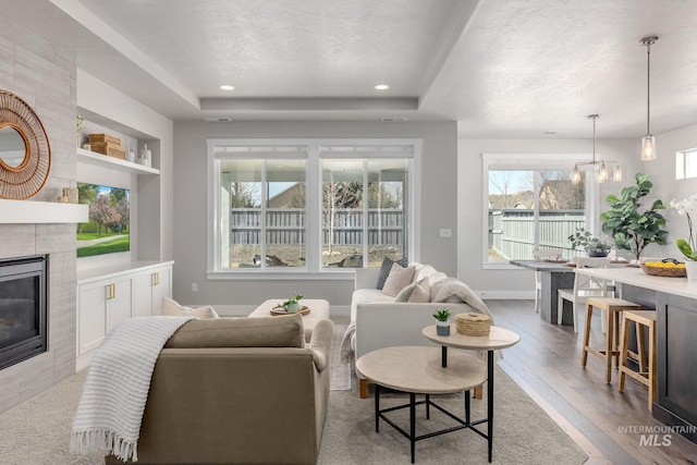 living area with built in shelves, a tray ceiling, a textured ceiling, wood finished floors, and a tile fireplace