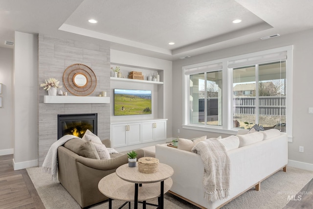 living room with a tiled fireplace, a raised ceiling, baseboards, and visible vents