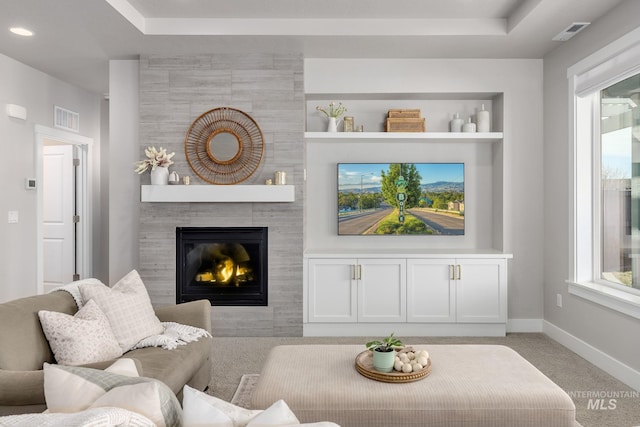 carpeted living area featuring visible vents, a fireplace, baseboards, and built in shelves