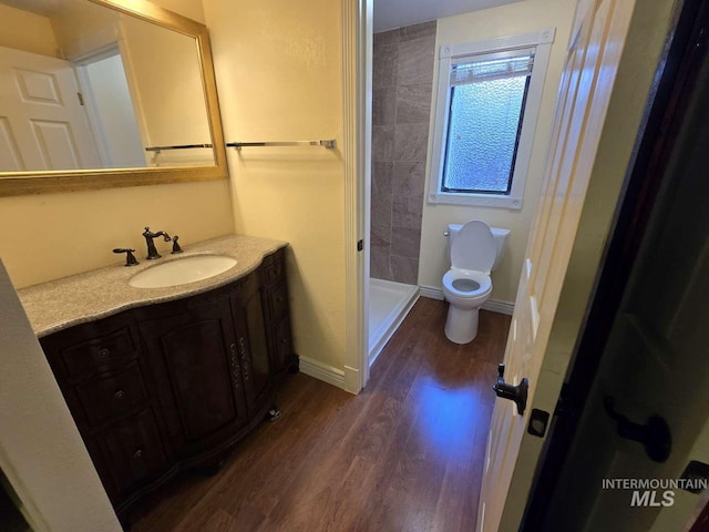 bathroom featuring hardwood / wood-style flooring, vanity, tiled shower, and toilet