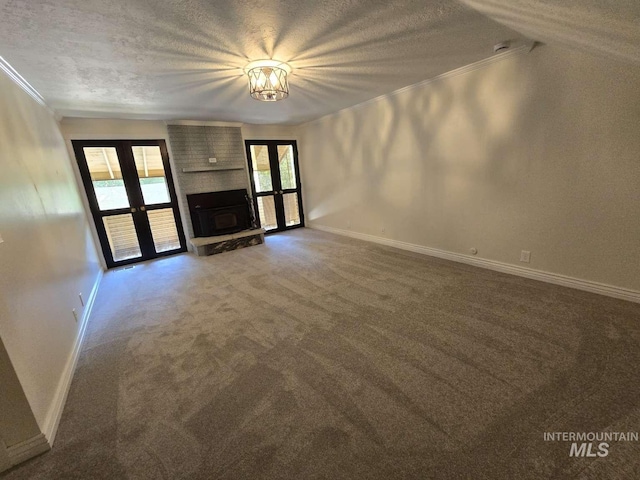 unfurnished living room featuring french doors, a textured ceiling, ornamental molding, carpet floors, and a fireplace