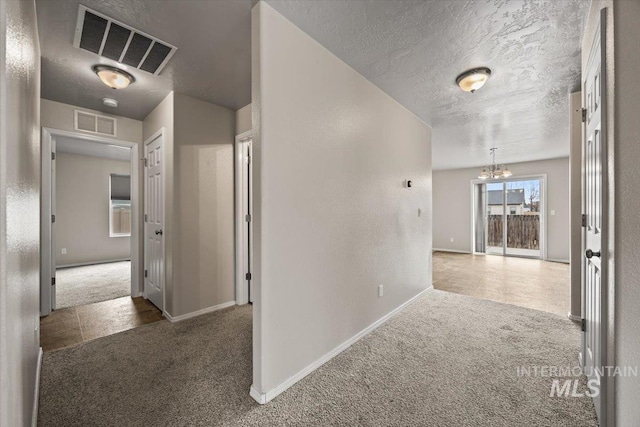 hall with dark colored carpet, a chandelier, and a textured ceiling