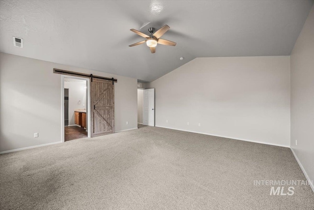 unfurnished bedroom featuring vaulted ceiling, ensuite bathroom, ceiling fan, dark carpet, and a barn door