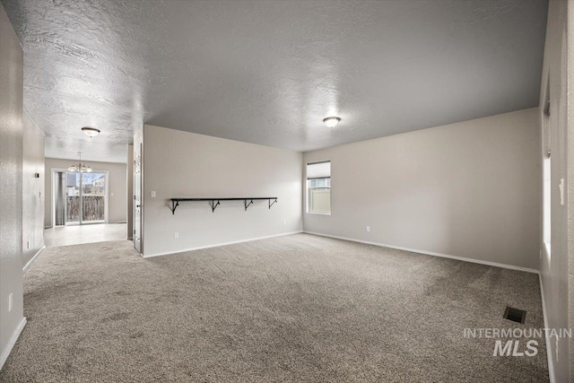 empty room featuring carpet flooring, a textured ceiling, and a chandelier