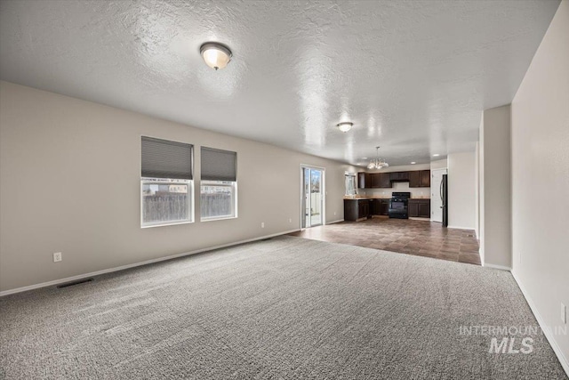 unfurnished living room featuring a notable chandelier, a textured ceiling, and dark colored carpet