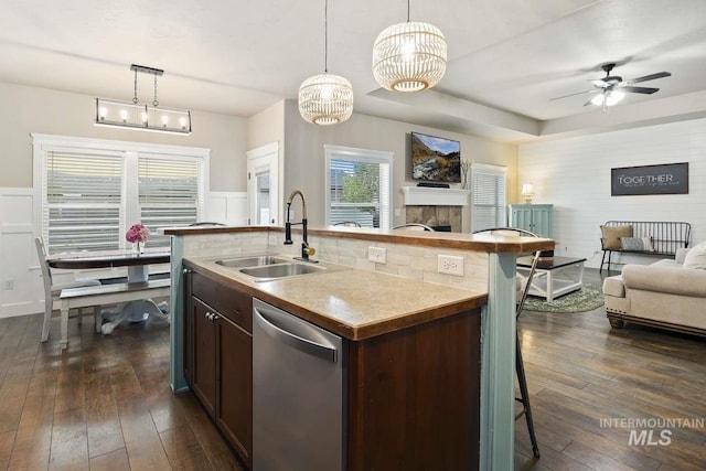 kitchen featuring a sink, open floor plan, dishwasher, dark brown cabinetry, and wainscoting