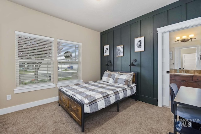bedroom featuring light carpet, a sink, baseboards, and ensuite bathroom