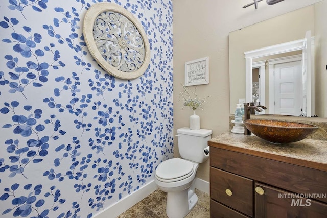 half bath featuring baseboards, vanity, and toilet