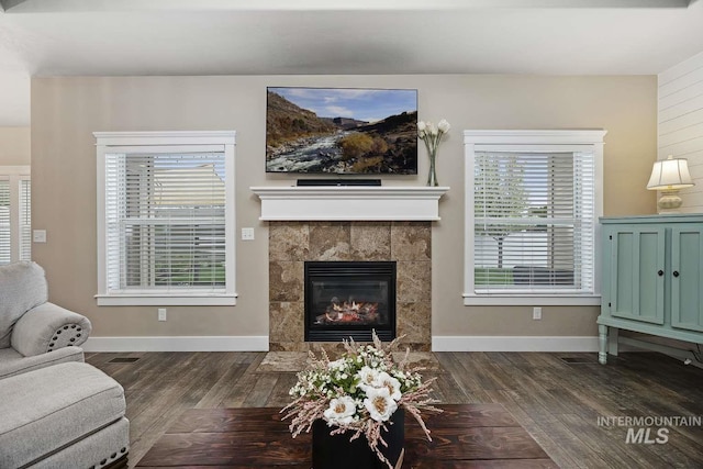 living room with dark wood-style floors, a tiled fireplace, and baseboards