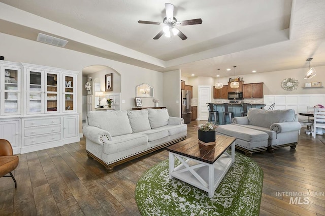living area with dark wood-style floors, a raised ceiling, ceiling fan, recessed lighting, and arched walkways