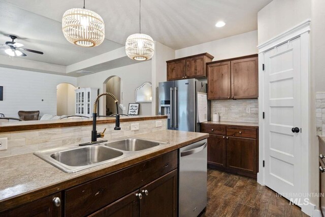 kitchen featuring appliances with stainless steel finishes, a sink, tasteful backsplash, pendant lighting, and arched walkways