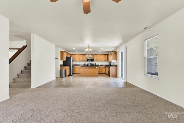 kitchen featuring open floor plan, stainless steel appliances, dark countertops, light colored carpet, and a chandelier