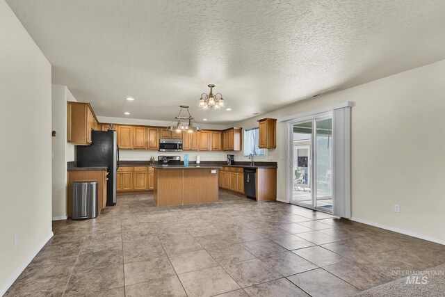 kitchen featuring appliances with stainless steel finishes, a chandelier, dark countertops, a center island, and a sink