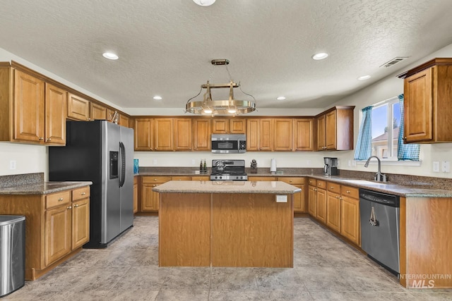 kitchen featuring appliances with stainless steel finishes, a sink, a kitchen island, a textured ceiling, and brown cabinets