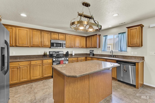 kitchen with stainless steel appliances, a sink, brown cabinetry, a kitchen island, and a textured ceiling