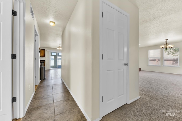 corridor with a chandelier, a textured ceiling, baseboards, carpet, and tile patterned flooring