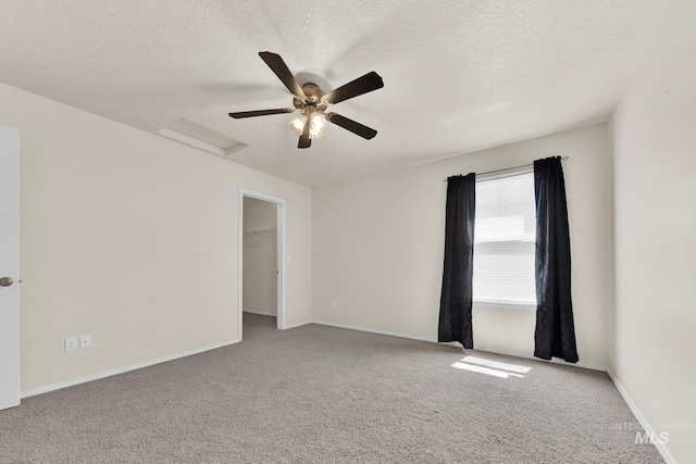 unfurnished room with attic access, carpet flooring, a textured ceiling, and baseboards