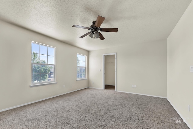 carpeted spare room with a textured ceiling, a ceiling fan, and baseboards