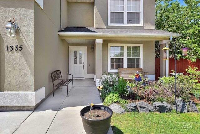doorway to property with covered porch, stucco siding, and fence