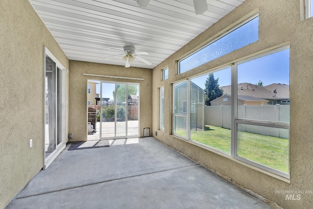 unfurnished sunroom featuring ceiling fan, a textured wall, and concrete flooring