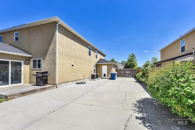 rear view of house featuring fence, stucco siding, a patio, central air condition unit, and a deck