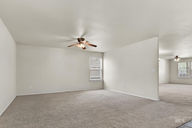 empty room featuring a ceiling fan, light colored carpet, a textured ceiling, and baseboards