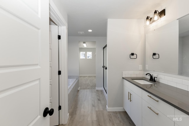 bathroom with vanity, wood finished floors, baseboards, a shower stall, and a garden tub