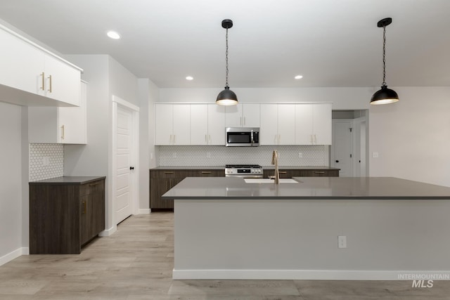 kitchen featuring an island with sink, a sink, appliances with stainless steel finishes, white cabinetry, and dark countertops