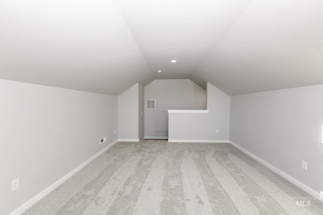 additional living space featuring visible vents, light colored carpet, baseboards, and lofted ceiling