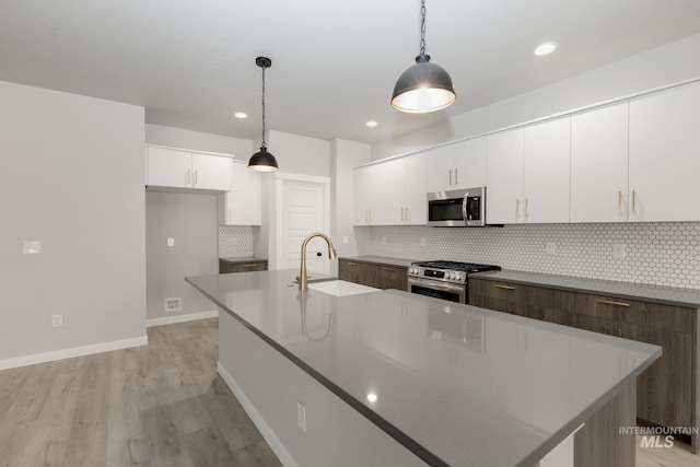 kitchen featuring a center island with sink, pendant lighting, appliances with stainless steel finishes, white cabinets, and a sink