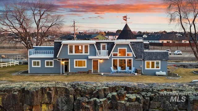 back of property featuring a balcony, mansard roof, and fence