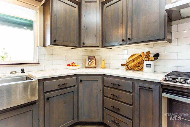 kitchen with decorative backsplash, dark brown cabinetry, stainless steel range oven, and light stone counters