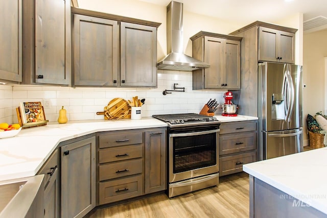 kitchen featuring light stone counters, wall chimney exhaust hood, backsplash, appliances with stainless steel finishes, and light wood-type flooring