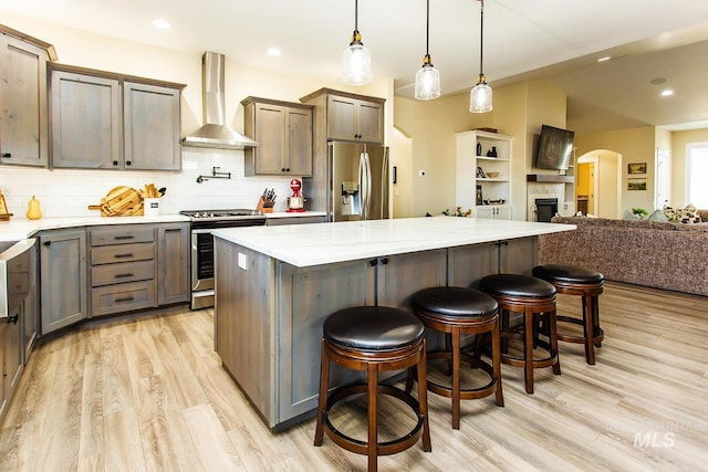 kitchen with wall chimney range hood, light hardwood / wood-style flooring, a breakfast bar, decorative light fixtures, and stainless steel appliances