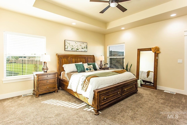 carpeted bedroom with multiple windows, ceiling fan, and a raised ceiling