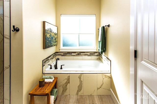 bathroom with tiled tub and wood-type flooring