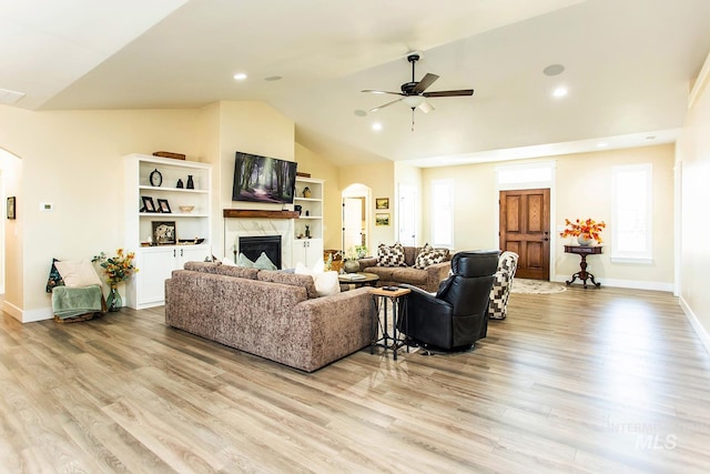 living room with ceiling fan, lofted ceiling, a premium fireplace, and light hardwood / wood-style flooring