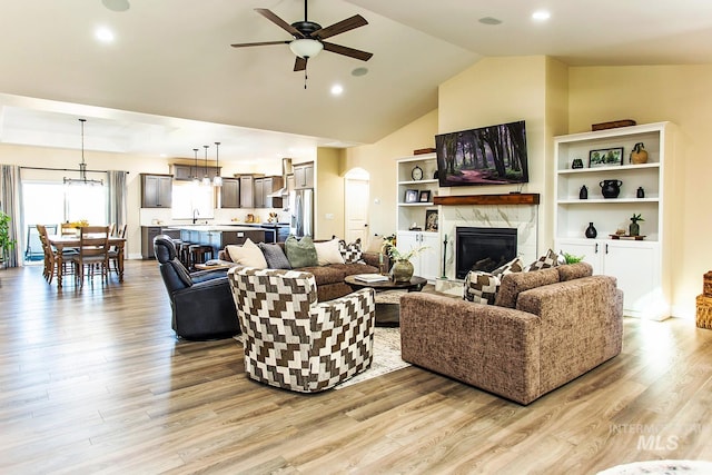 living room with light hardwood / wood-style floors, ceiling fan, a premium fireplace, sink, and high vaulted ceiling