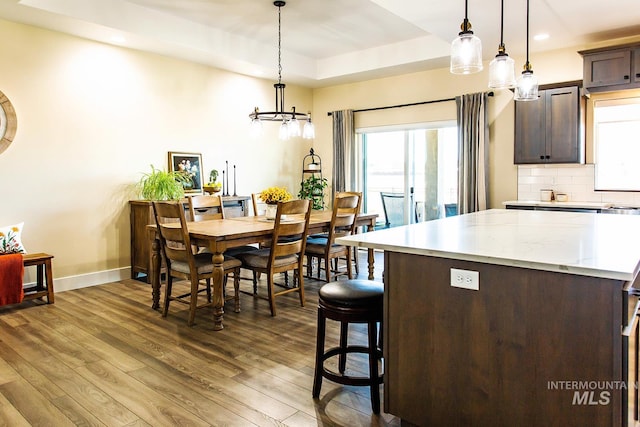 kitchen featuring dark brown cabinetry, hanging light fixtures, a tray ceiling, and wood-type flooring