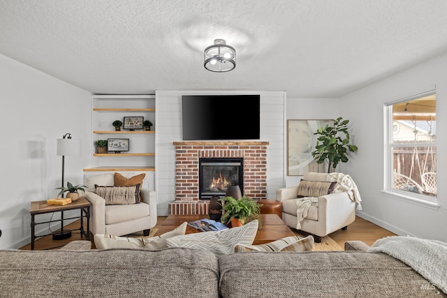 living area featuring a fireplace, a textured ceiling, baseboards, and wood finished floors